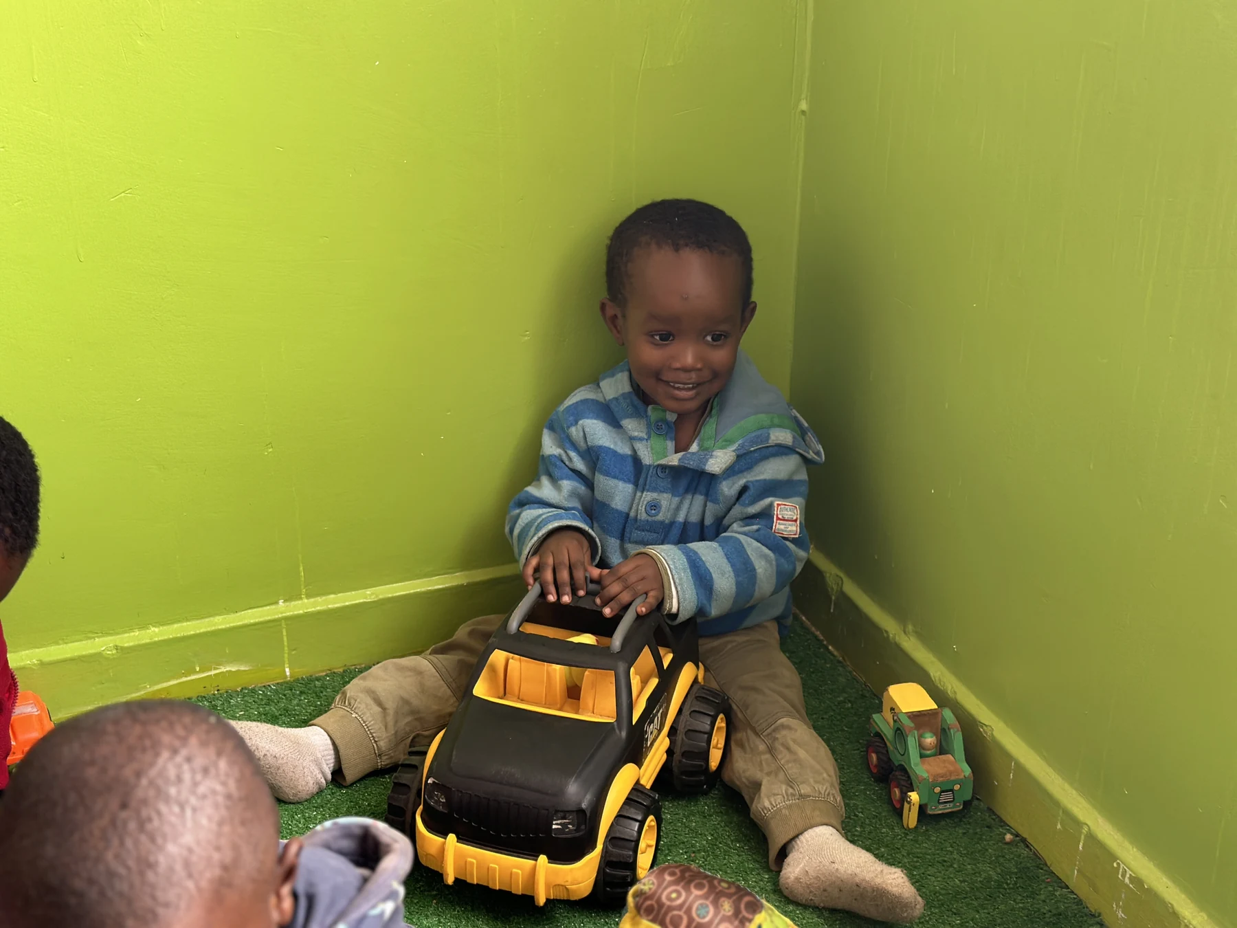 A smiling child playing with a large toy truck in the playroom
